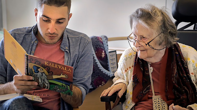 A man reads Kalevala out loud, an elderly woman listens.