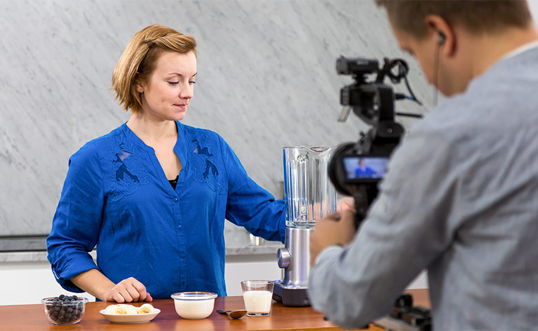 Nainen valmistaa juomaa. Mies kuvaa videota.